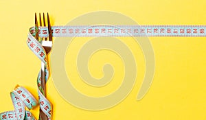 Diet and healthy eating concept with fork and measuring tape on yellow background. Top view of weightloss