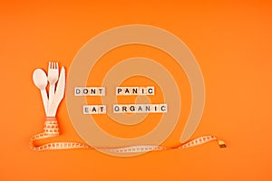 Diet and healthy eating concept - wooden cutlery, yellow measuring tape and words DONT PANIC EAT ORGANIC on wooden bricks, on