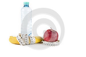 Diet, healthy eating, food and weigh loss concept - close up of banana apple and measuring tape.