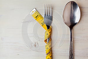 Diet  light wooden background  fork wrapped in a meter  fork and spoon on a white background