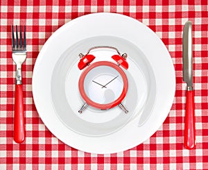 Diet lunch time concept.Red alarm clock on round white plate.