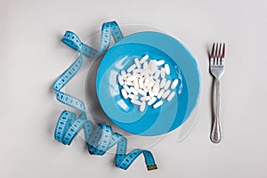 Diet pills on blue plate and tape on gray background