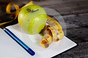 Diet plan, empty notebook, pencil, green apple and measuring tape, flat lay on wooden background