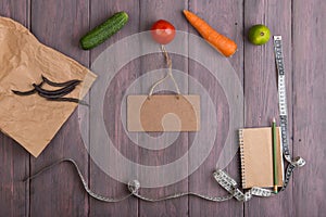 Diet plan and food diary concept - measure tape, blank notebook and blackboard, paper eco bag with healthy various vegetables