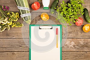 marrow squash, measure tape, blank clipboard, bottle of water, flowers, tomatoes and cucumbers on brown wooden table