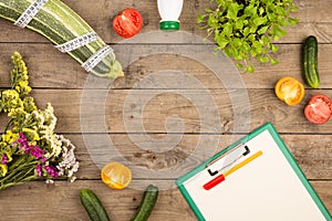 marrow squash, measure tape, blank clipboard, bottle of water, flowers, tomatoes and cucumbers on brown wooden table