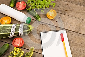 marrow squash, measure tape, blank notepad, bottle of water, flowers, tomatoes and cucumbers on brown wooden table