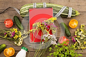 marrow squash, measure tape, blank red notepad, bottle of water, flowers, tomatoes and cucumbers on brown wooden table