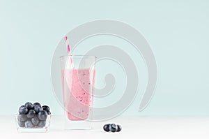 Diet purple milk beverage in elegant glass with striped straw, blueberry in bowl on pastel soft light blue background, copy space.