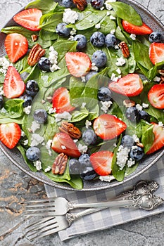 Diet salad with spinach, berries such as strawberries, blueberries with cheese and pecans and honey dressing close-up in a plate