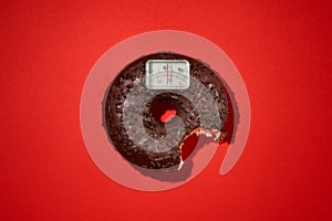 Diet slimness weight loss scale scales chocolate coated doughnut bitten on a red background