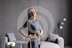 Diet, sport and heath concept - beautiful sporty woman with measuring tape at home