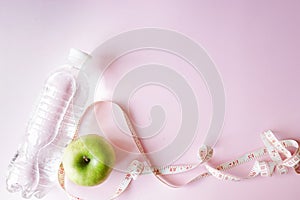 Diet symbol flat lay one meter ribbon and apple and a bottle of water. pink background with copy space. health sport concept
