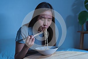 Diet, templtation. Alone asian young student woman, girl using chopsticks eating instant ramen, noodles in bowl on table in