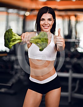Diet and weight loss concept. Happy smiling athletic girl fitness instructor handed us big broccoli and show thumb up sign