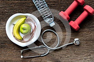 Diet and weight loss for healthy care with medical stethoscope, fitness equipment,measuring tap,fresh water and green apple on woo