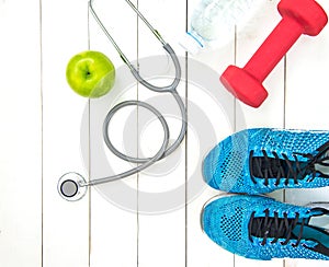 Diet and weight loss for healthy care with medical stethoscope, fitness equipment,measuring tap,fresh water and green apple on woo