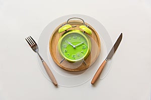 Diet and weight loss for healthy intermittent fasting lunchtime . Alarm clock and plate with cutlery on concrete background.