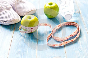Diet and weight loss with measuring tap, green apple, water and sneakers for fitness on blue wooden background top view