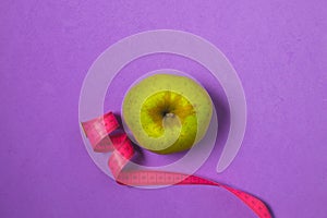 Diet, weight loss minimal concept, healthy - green apple, pink measuring tape, top view, copy space, purple background