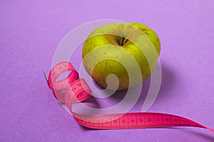 Diet, weight loss minimal concept, healthy - green apple, pink measuring tape, top view, copy space, purple background