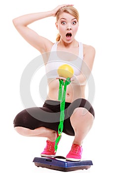 Diet weightloss. Surprised woman on scale holds fruit measuring tape