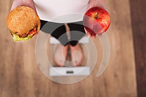 Diet. Woman Measuring Body Weight On Weighing Scale Holding Burger and apple. Sweets Are Unhealthy Junk Food. Dieting, Healthy Eat