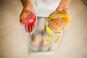 Diet. Woman Measuring Body Weight On Weighing Scale Holding Burger and red apple. Sweets Are Unhealthy Junk Food. Weight