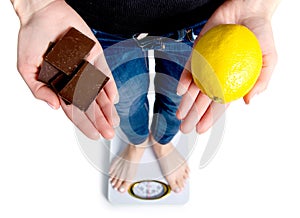 Diet. Woman Measuring Body Weight On Weighing Scale Holding chocolate and lemon.