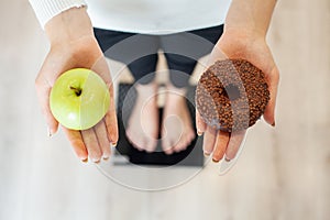 Diet. Woman Measuring Body Weight On Weighing Scale Holding Donut and apple. Sweets Are Unhealthy Junk Food. Dieting