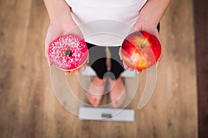 Diet. Woman Measuring Body Weight On Weighing Scale Holding Donut and apple. Sweets Are Unhealthy Junk Food. Dieting, Healthy Eat