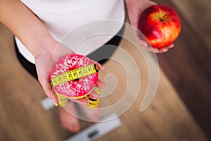 Diet. Woman Measuring Body Weight On Weighing Scale Holding Donut and apple. Sweets Are Unhealthy Junk Food. Dieting, Healthy Eat