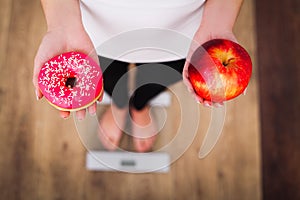 Diet. Woman Measuring Body Weight On Weighing Scale Holding Donut and apple. Sweets Are Unhealthy Junk Food. Dieting, Healthy Eat