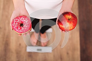 Diet. Woman Measuring Body Weight On Weighing Scale Holding Donut and apple. Sweets Are Unhealthy Junk Food. Dieting, Healthy Eati