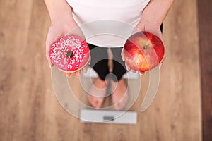 Diet. Woman Measuring Body Weight On Weighing Scale Holding Donut and apple. Sweets Are Unhealthy Junk Food. Dieting, Healthy Eati