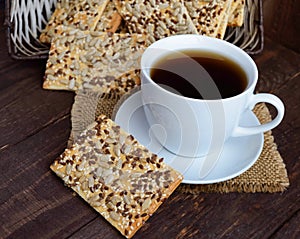 Dietary crunchy cracker with cereals (sunflower seeds, flax and sesame) and a cup of tea on a dark