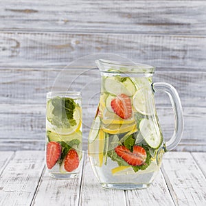 Dietary detox drink with lemon juice, red strawberry, cucumber and mint leaves in clear water with ice.