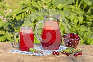 Dietary detox drink with red cherry in clear water with ice. Cherry juice in jug and in glass and ripe cherries in plate