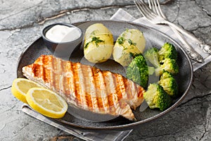 Dietary grilled salmon with boiled potatoes, broccoli, lemon, herbs and cream sauce close-up in a plate. Horizontal