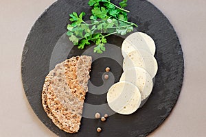 Dietary homemade chicken mortadella with allspice on slate board. Protein rye multicereal flatbread. Gray background.