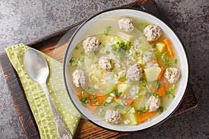 Dietary Rice meatball soup with celery, carrots, onions, potatoes and herbs close-up in a bowl. Horizontal top view