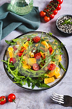 Dietary salad of orange slices, cherry tomatoes and arugula on a plate on the table vertical view