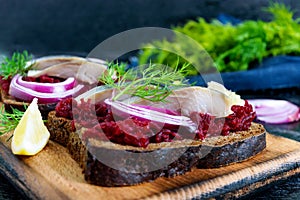 Dietary sandwiches with beets, slices of salted herring and red onion on rye bread on a black background