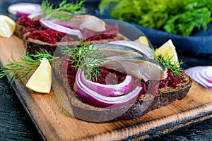 Dietary sandwiches with beets, slices of salted herring and red onion on rye bread on a black background