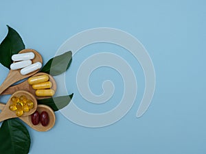 Dietary supplements, vitamins, tablets, capsules, minerals in wooden spoons and green leaves near on a blue background