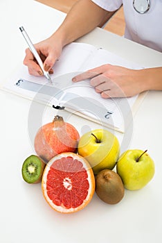 Dietician writing prescription with fruits on desk photo