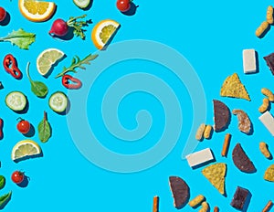 Dieting choices concept with healthy fruits and vegetables and junk food on opposite sides with copy space on blue background