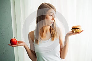 Dieting concept, beautiful young woman choosing between healthy food and junk food