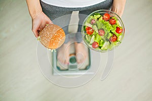 Dieting concept, beautiful young woman choosing between healthy food and junk food