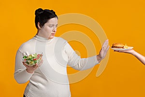 Overweight girl refusing fast food, holding bowl with fresh vegetable salad